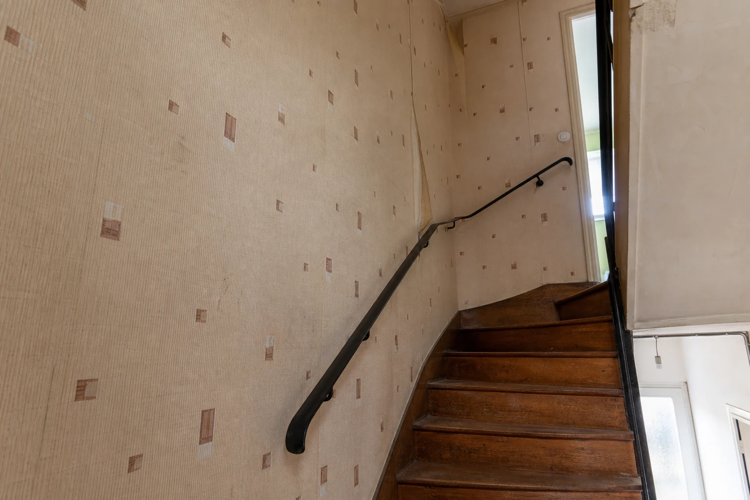 Cage d’escalier avant rénovation avec ancien papier peint beige décollé par endroits