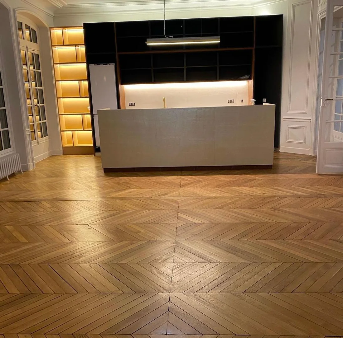 Cuisine ouverte avec îlot central, bibliothèque rétroéclairée et parquet en point de Hongrie dans un appartement haussmannien
