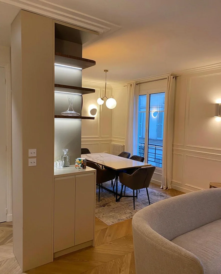 Cuisine ouverte prolongée par une salle à manger, étagères éclairées et parquet en chevrons