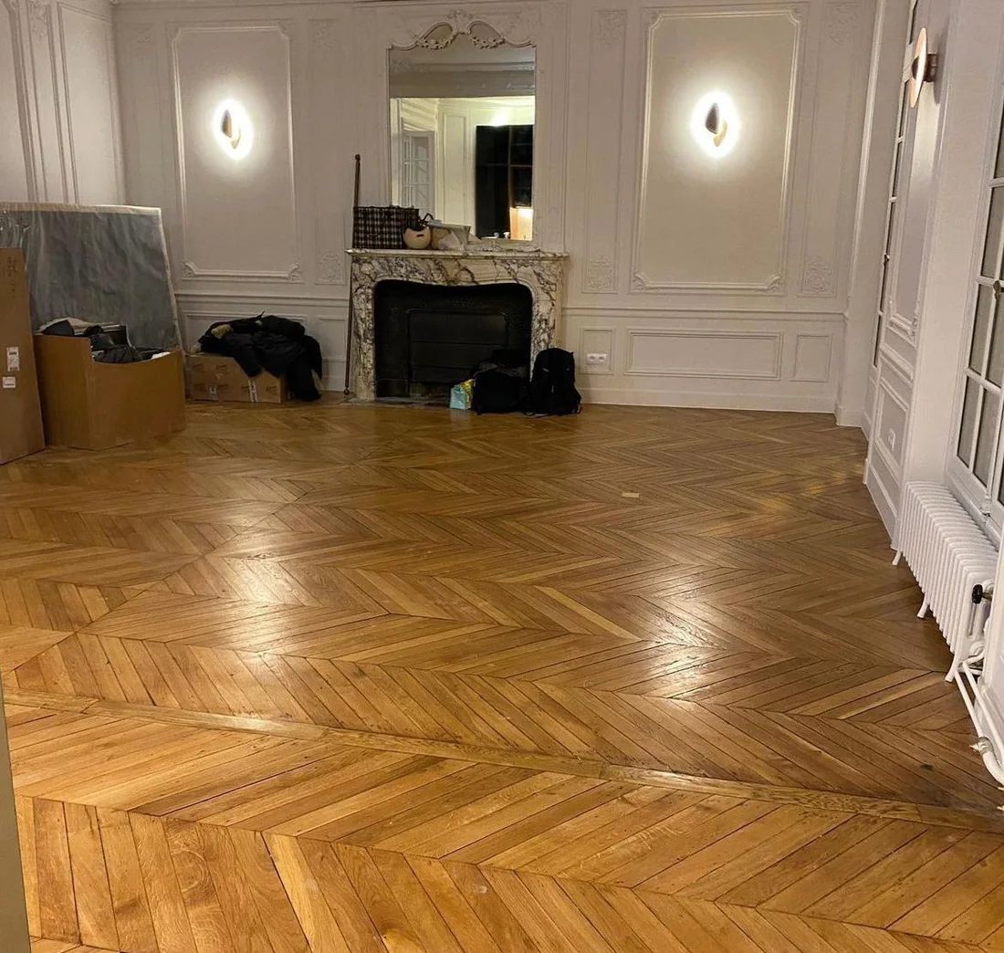 Salon aux murs moulurés blancs, cheminée en marbre et parquet ancien en point de Hongrie
