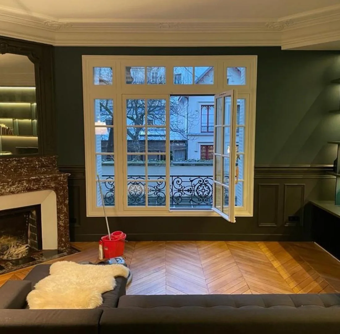 Salon aux murs vert profond avec soubassement mouluré, cheminée en marbre et fenêtre à petits bois